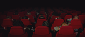 Rows of red chairs in a cinema screen, with people watching a movie