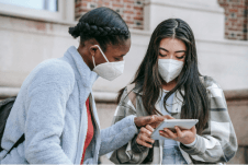 Two people wearing protective face masks using a tablet device outside